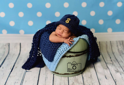 newborn baby boy in blue bucket hat and polkadot backdrop