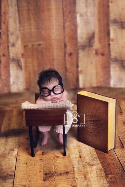newborn baby photographer baby sitting at desk with glasses and book
